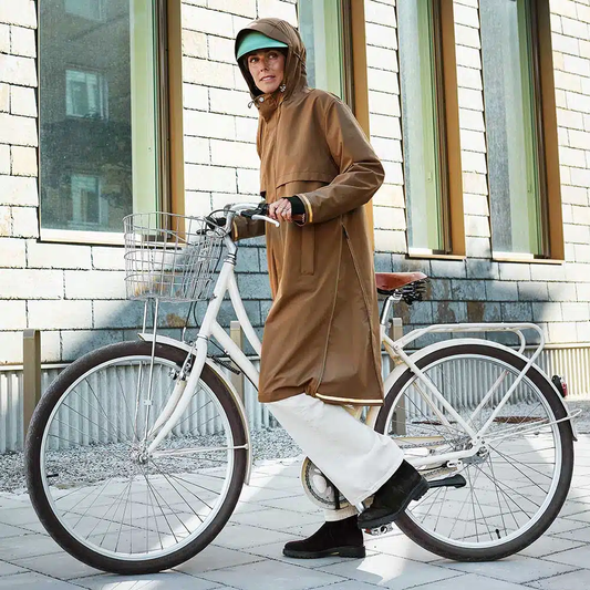 Frau im Regenmantel mit Fahrrad in der Stadt – wasserdichte Fahrradtasche für jeden Wetter
