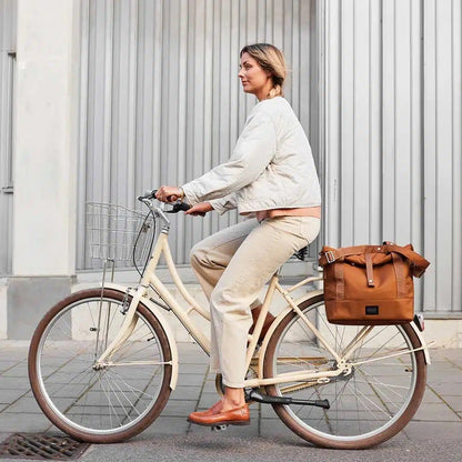 Frau fährt Fahrrad in der Stadt mit City Bike Satchel braun am Gepäckträger – Weathergoods Sweden
