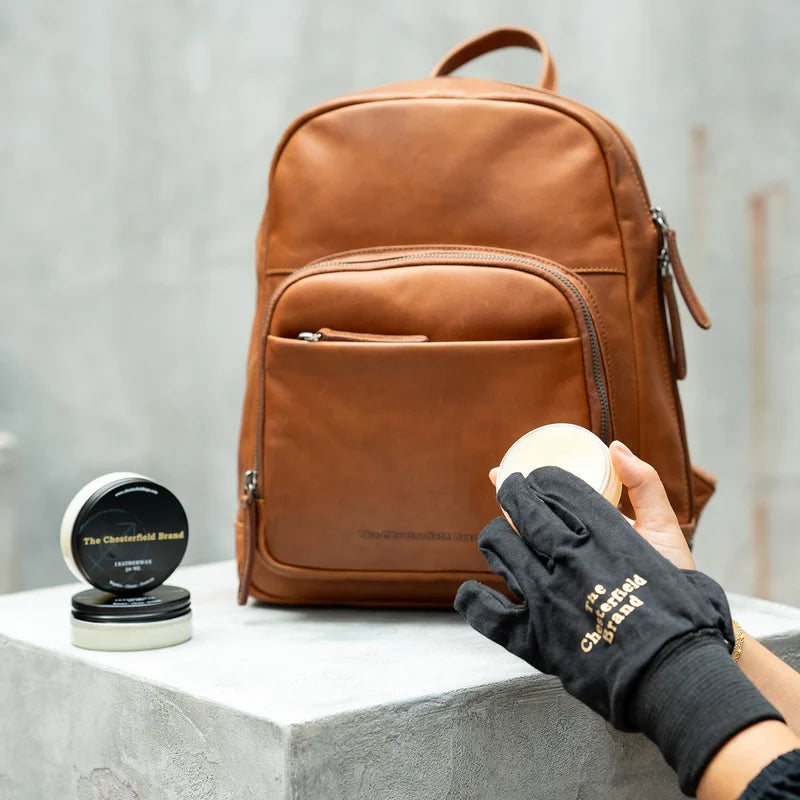 Lederpflege mit The Chesterfield Brand Lederwachs – Hand mit Handschuh pflegt cognacfarbenen Lederrucksack